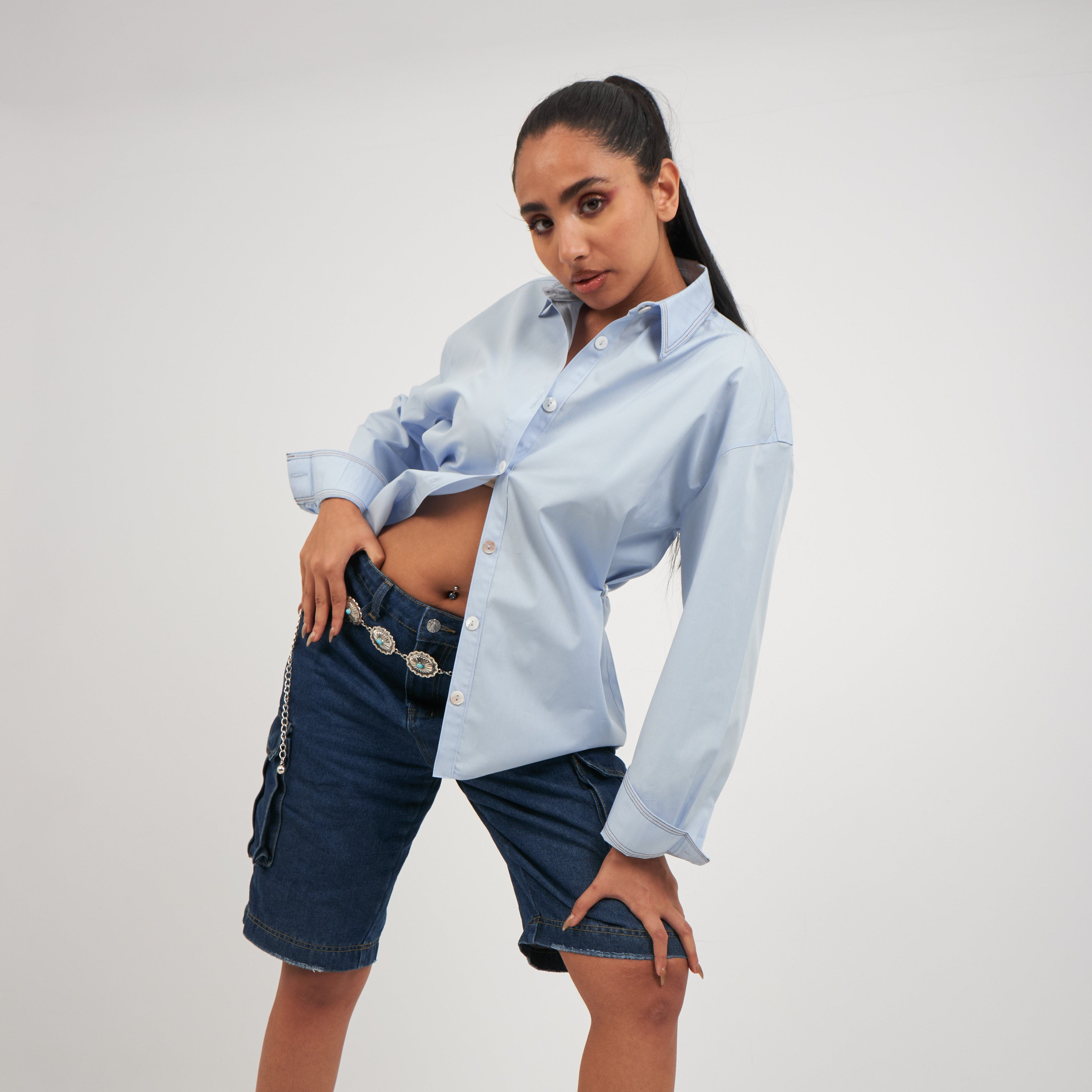 Woman wearing a light blue shirt and dark denim shorts on a white background